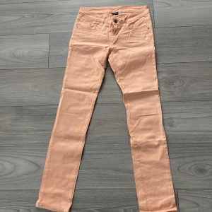 Lågmidjade persikofärgade skinny jeans  - Snygga persikofärgade skinny jeans med klassiska fem fickor och bälteshällor. Byxorna är i stretchig bomull och har en smal passform som sitter tajt längs benen. Perfekta för dig som vill ha en fräsch och trendig look. (Byxorna är lite mörkare i verkligheten)