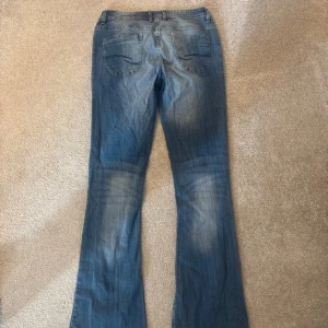 Blå flared jeans från Peak Motion - Snygga blå jeans från Peak Motion i klassisk flared-modell. Jeansen har normal midja, fem fickor och coola slitningar för en avslappnad vibe. Tillverkade i mjukt denimtyg som sitter skönt hela dagen.