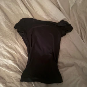 Svart tight topp med öppen rygg - Säljer en svart, tight topp med korta ärmar och en djup, öppen rygg. Toppens minimalistiska design gör den enkel att styla och den sitter snyggt figurnära. Perfekt för dig som gillar en clean och stilren look.