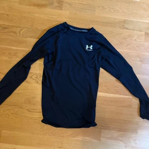 Svart långärmad träningströja Under Armour - Säljer en svart långärmad träningströja från Under Armour. Tröjan är i ett stretchigt och lätt material som andas, perfekt för intensiva träningspass. Diskret logga på bröstet och en reflexdetalj på ryggen. Snygg och sportig passform.