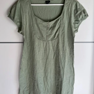 Ljusgrön blus från Cellbes - Ljusgrön blus från Cellbes med korta puffärmar och rundad halsringning. Framsidan har dekorativa veck och små knappar som ger en söt touch. Tillverkad i mjuk bomull, perfekt för en chill och avslappnad stil.