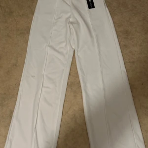 Vita vida kostymbyxor - Snygga vita kostymbyxor med vida ben och pressveck. Perfekta för en clean och stilren look. Byxorna har hög midja och är gjorda i ett mjukt material som känns bekvämt hela dagen
