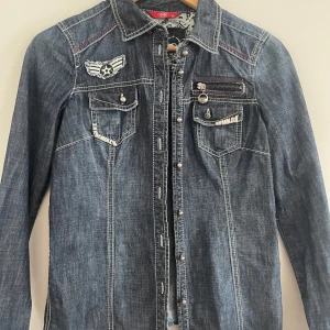 Jeansskjorta från edc by Esprit XS - Snygg jeansskjorta från edc by Esprit i mörkblå denim med coola detaljer som bröstfickor, dekorativ dragkedja och broderad patch. Skjortan har långa ärmar, tryckknappar och kontrastsömmar. Perfekt för dig som gillar en avslappnad men edgy stil.