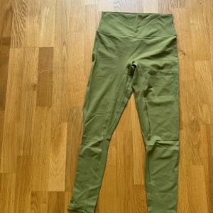 Olivgröna höga träningstights  - Snygga olivgröna träningstights med hög midja och tight passform. Perfekta för träning eller chill, i mjukt och stretchigt syntetmaterial som sitter skönt hela dagen.