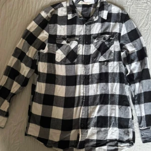 Svartvit rutig skjorta från H&M - Klassisk svartvit rutig skjorta från H&M i storlek 170. Skjortan har två bröstfickor med knappar, långa ärmar och en avslappnad passform. Perfekt att bära öppen över en t-shirt eller stängd för en mer stilren look.