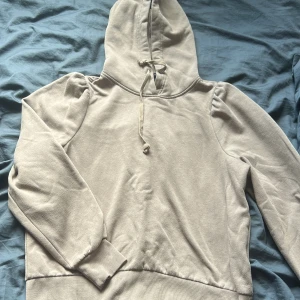 Beige hoodie från PIECES med puffärm - Säljer en beige hoodie från PIECES i storlek M. Tröjan har puffiga axlar, huva med snörning och ribbade muddar. Perfekt för dig som gillar en chill och trendig look. Materialet är mjukt och skönt, troligtvis bomullsmix.