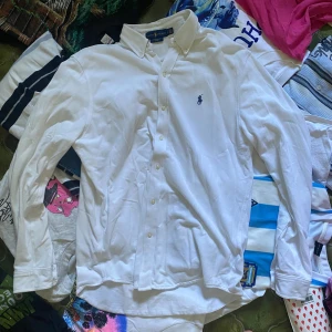 Vit skjorta från Ralph Lauren  - Vit långärmad skjorta från Ralph Lauren i mesh-bomull. Klassisk button-down krage, knappar framtill och broderad blå logga på bröstet. Skjortan har en normal passform och är perfekt för en clean och stilren look. Nypris 1295 :- 