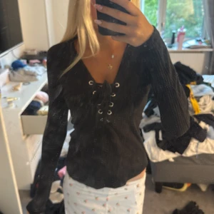 Svart ribbad tröja med snörning Gina Tricot - Svart långärmad tröja från Gina Tricot i ribbat material. Snygg v-ringning med snörningsdetalj framtill som ger en trendig look. Figurnära passform och tyg som sitter skönt på kroppen. Perfekt till jeans eller kjol för en cool vardagsstil. 🥰