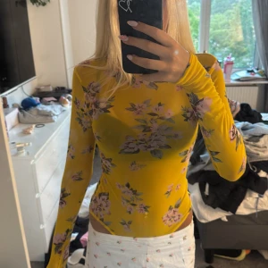 Gul mesh blommig långärmad body - Säljer en superfin gul mesh topp med lång ärm och blommigt mönster i rosa och lila toner. Bodyn är tight och genomskinlig, perfekt att styla med ett linne under eller som den är för en trendig look. Aldrig använd💓