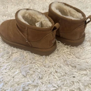 Chestnut UGG boots - barn - Mysiga bruna mini UGG boots för barn  i mocka med fluffigt vitt fårfoder på insidan. Perfekta för kalla dagar 