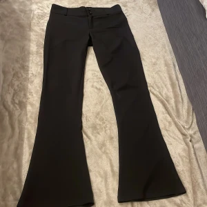 Svarta kostym bootcut byxor Gina Tricot M - Svarta kostymbyxor från Gina Tricot i storlek M (kan funka som S). Byxorna är använda en gång och har låg midja, två knappar framtill och är tillverkade i ett mjukt, stretchigt material. Snygg passform med utsvängda ben som ger en trendig siluett.