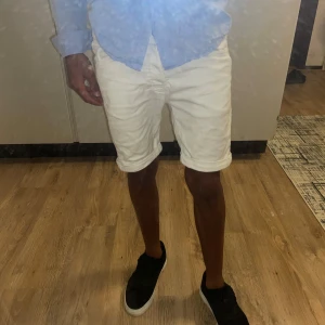 Vita shorts med uppvikta ben - Snygga vita shorts med klassisk femficksmodell och uppvikta ben. De har normal passform och är perfekta för varma dagar. Stilen är enkel och fräsch, passar till skjorta eller t-shirt. Materialet känns som bomull och de har diskreta sömmar och knappar framtill.