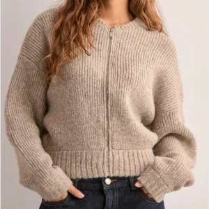 Beige stickad kofta med dragkedja - Supermysig beige stickad kofta med dragkedja framtill. Koftan har ribbade muddar och midja, samt långärmad och loose fit. Perfekt för lager-på-lager och chill dagar. Enkel och stilren design som passar till jeans eller kjol.