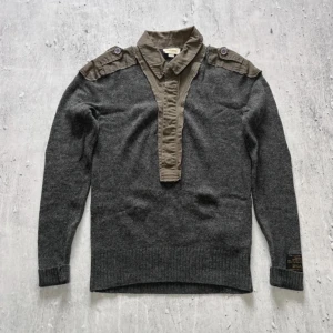 Stickad militär tröja från diesel - Säljer denna unika stickade tröja från Diesel med tydlig militär- och techwear-känsla.  Tillverkad i en mörkgrå ullmix med kontrasterande olivgröna bomullspaneler vid axlarna och kragen – ger en militär uniform-look kombinerat med Diesels ikoniska tidiga 2000-talsstil. Ett riktigt arkivplagg – svår att hitta   Märkt M – passar som en lång/slim M  