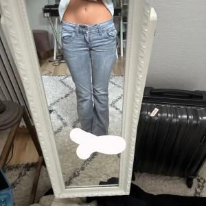 Grå bootcut jeans med fickdetaljer - Säljer ett par grå jeans med bootcut-modell och snygga fickdetaljer både fram och bak. Jeansen har låg midja och är tillverkade i klassiskt denimtyg. Perfekta för dig som gillar en avslappnad men ändå trendig look. Väldigt låga