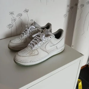Nike Air Force 1 vita sneakers - Klassiska Nike Air Force 1 sneakers i vitt skinn med perforerad tå och vit sula. Lågt skaft, snörning och diskret Nike-logga på sidan. Perfekta för dig som gillar en clean och tidlös streetstil. Storlek 43. Orginal snören kommer med också.