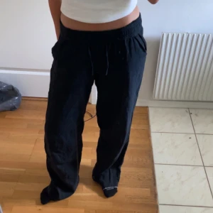 Svarta linnebyxor med snörning - Säljer ett par svarta linnebyxor med avslappnad passform och resår i midjan. Byxorna har snörning och sidfickor, perfekta för en chill och stilren look. Lätta och luftiga, passar grymt till sommaren. Strl 36-38, Aldrig använda 