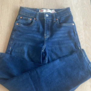 Levi's blå jeans med cargofickor - Snygga mörkblå jeans från Levi's med klassiska kontrastsömmar och stora cargofickor på benen. Modellen har fem fickor, bälteshällor och Levi's ikoniska läderpatch bak. Tillverkade i slitstarkt bomullsjeansmaterial. Ny pris var 600 kr, använda 1 gång, säljs nu för 150 kr