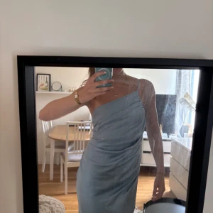 Ljusblå långklänning med oneshoulder - Säljer en ljusblå långklänning i satin med oneshoulder och öppen rygg. Klänningen har en jättefin passform och ett vackert fall. Perfekt för bal eller fest! Klänningen är helt oanvänd och har fortfarande prislappen kvar! 💙 