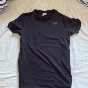 Svart t-shirt från Gymshark - Säljer en svart t-shirt från Gymshark i storlek S. Den har en stilren design med korta ärmar och Gymsharks logga tryckt på bröstet. Perfekt för träning eller en avslappnad look.