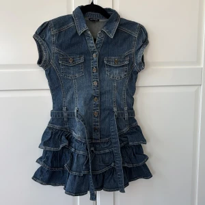Jeansklänning med volanger från KappAhl - Säljer en snygg jeansklänning från KappAhl med korta ärmar, knappar framtill, två bröstfickor och volanger nertill. Klänningen har ett bälte i midjan, passar perfekt till sommaren!💓