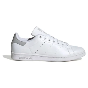 Vita Adidas Stan Smith sneakers - Klassiska vita Adidas Stan Smith sneakers med diskreta perforerade ränder på sidorna och silverdetaljer på hälen. Skorna har snörning och är tillverkade i syntetmaterial med platt sula och rund tå. Perfekta för en clean och stilren look.