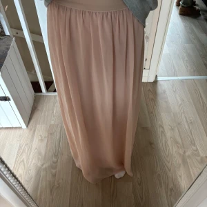  långkjol  - Säljer en ljusrosa långkjol med mjukt fall och resår i midjan. Kjolen har en enkel och stilren design som passar perfekt till många olika outfits. Superbekväm och lätt att matcha med både sneakers och sandaler.