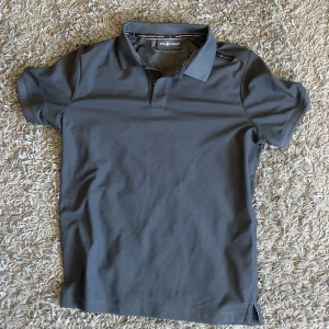 Mörkgrå pikétröja från Sail Racing - Säljer en stilren mörkgrå pikétröja från Sail Racing. Det är en perfekt dag om man ska iväg och träna fast i piké för det är ett skönt och sportigt material, hör av er! 