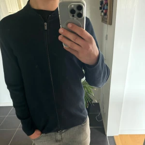 Mörkblå stickad kofta från Massimo Dutti - Säljer en stilren mörkblå stickad kofta från Massimo Dutti med dragkedja framtill. Tröjan har lång ärm och ribbade muddar vid hals, ärmslut och nederkant. Perfekt för lager-på-lager och passar till många tillfällen. Tröjan är aldrig använd mer än i butik vilket leder till ett skick som nytt. Storleken är M men passar även S hör av er för eventulla frågor!!