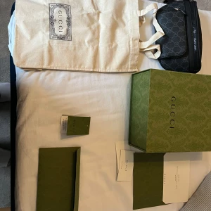 Gucci midjeväska - Säljer en snygg svart axelväska från Gucci med diskret GG-mönster och svarta detaljer. Väskan har justerbar axelrem och dragkedja upptill. Kommer med originalförpackning, dustbag och äkthetskort. Perfekt för dig som vill ha en stilren och lyxig accessoar. Otroligt bra skick, inga skador eller liknande. För mer frågor kom dm! Pris går att diskutera vid en snabb och smidig affär.
