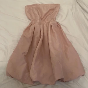 Ljusrosa axelbandslös klänning från ONLY - Säljer en söt ljusrosa axelbandslös klänning från ONLY med vidd i kjolen och smock baktill för extra komfort. Perfekt för sommarens tillfällen och enkel att styla med accessoarer.