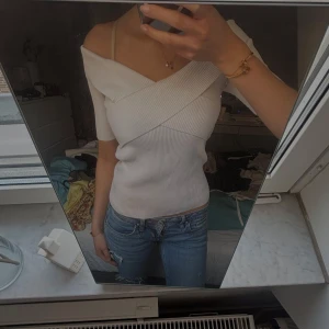 Vit omlottopp med ribbad struktur - Säljer en vit omlottopp med ribbad struktur och kort ärm. Toppen har en snygg omlottdesign över bysten och en smickrande passform. Perfekt att styla med jeans eller kjol.