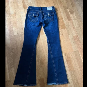 True Religion Joey Low Rise Flare Jeans - Mörkblå jeans från True Religion i storlek 26, modell Joey Low Rise Flare. Byxorna har låg midja, utsvängda ben och dekorativa fickor bak. Dom är använda få gånger och nästan nyskick.
