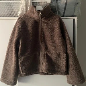 Brun teddyjacka  - Mysig brun teddyjacka från 157 med hög krage och dragkedja framtill. Jackan har två stora fickor och är tillverkad i ett fluffigt teddy-material som håller dig varm under kyliga dagar. Perfekt nu till våren när de inte är jätte kallt men inte jätte varmt! Den är bara provad, då jag köpte fel storlek! Storlek L men dom är väldigt små i storleken, skulle säga att den passar M/S. Kan tänka mig sänka ganska mkt men bara snabb affär ingen pris förslag sen sluta svara tack. 