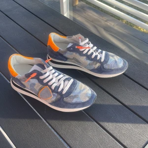 Philippe Model sneakers med camomönster och orange detaljer - Säljer ett par Philippe Model sneakers med unikt camomönster. Storlek 41, säljer för att de inte passar. Box och dustbags ingår såklart.