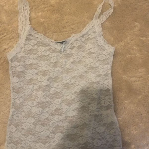  spetslinne från Brandy Melville - Säljer ett vitt spetslinne från Brandy Melville med smala axelband och liten rosett framtill. Hela linnet är gjort i genombruten spets med blommigt mönster. Perfekt att styla lager på lager.