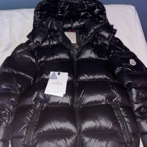 Svart pufferjacka från Moncler - Säljer en svart pufferjacka från i vintras, väldigt fint skick i övrigt förutom det lilla hålet på armen men inget man tänker på och det åker inte ut nått. Säljer då jag ska köpa cardigan har du nån fråga bara fråga