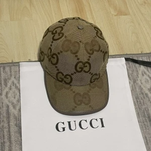 Beige keps från Gucci med GG-mönster - Säljer en beige keps från Gucci med det klassiska GG-mönstret i brunt. Kepsen har böjd skärm och justerbar rem baktill. Perfekt accessoar för dig som gillar lyxiga märken och stilren design.