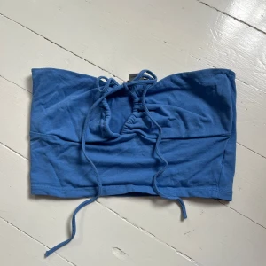 Blå tubtopp med knyt från Monki - Säljer en blå tubtopp från Monki med knyt framtill. Toppen är ärmlös och har en enkel, stilren design i mjukt bomullsmaterial. Kan även knytas runt nacken på olika sätt. Perfekt att matcha med jeans eller kjol för en avslappnad look. Om du köper flera kan du få ett bra pris. Skriv för fler bilder💙