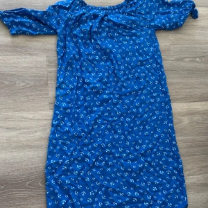 Blå klänning med ankarmönster - Säljer en blå klänning med små vita ankare som mönster. Klänningen har korta ärmar och en lös passform, perfekt för varma dagar. Rund halsringning och lätt, luftig känsla.