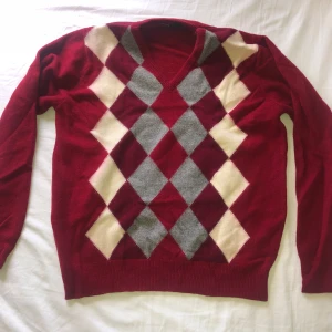 Röd vintage argyletröja  - Säljer en röd argyletröja från Alan Paine i 100% lammull. Tröjan har v-ringning och ett rutigt mönster i grått, rött och vit framtill. (Färgen har spritt lite som man ser i bild 4)