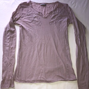 Ljuslila långärmad topp från Hunkydory - Säljer en ljuslila långärmad topp från Hunkydory med broderade detaljer framtill och lätt v-ringad hals. (Lite hål på baksidan vid etikketen som man ser på bild 4, tror den e storlek m)