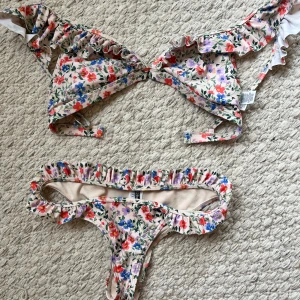 Blommig bikini med volangdetaljer - Söt bikini med blommigt mönster i rosa, rött, blått och grönt. Både överdel och underdel har volang längs kanterna. Bikinin har smala axelband och knyt i ryggen. Perfekt för sommardagar på stranden. Kom privat för bättre bilder 💕