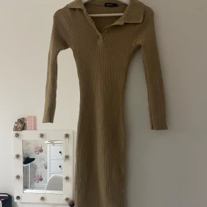 Beige ribbad långklänning med krage från Boohoo - Säljer en beige ribbad långklänning från Boohoo med lång ärm och klassisk krage. Klänningen har knappar framtill vid halsen och är figurnära i modellen. Perfekt för dig som gillar stilrena och enkla plagg.