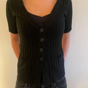 Svart ribbad kofta med kort ärm - Svart ribbad kofta med korta ärmar och djup v-ringning. Snygg och enkel att styla till olika outfits.