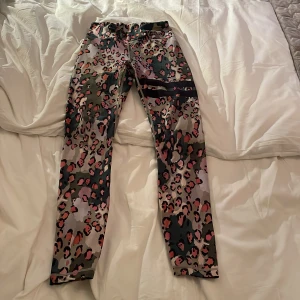 Leopardmönstrade tights från Stronger - Säljer ett par snygga tights från Stronger med leopardmönster i rosa, svart och grönt. De har hög midja och är i stretchigt syntetmaterial, perfekta för träning eller när du vill sticka ut lite extra.