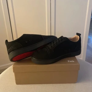 Christian Louboutin - Säljer ett par svarta sneakers från Christian Louboutin med klassisk röd sula. Skorna har snörning, rund tå och är tillverkade i mocka med svarta detaljer. Insidan är ljusbeige och baksidan har broderad logga. Perfekta för sommar ☀️ 