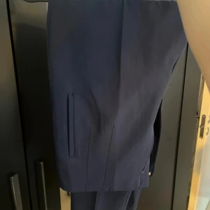 Mörkblå kostymbyxor - Snygga mörkblå kostymbyxor med raka ben och diskreta fickor på sidorna. Perfekta för en dressad look och passar till skjorta eller kavaj. Klassisk design utan synliga detaljer för en stilren känsla.