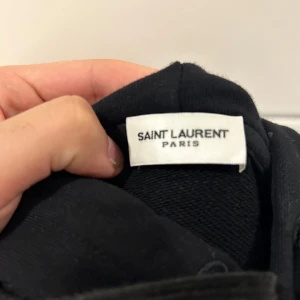 Svart hoodie från Saint Laurent - Säljer min Saint Laurent hoodie Använd en gång, i stort sett som ny! Storlek S. Riktigt snygg och stilren – passar till allt. Säljer bara för att den inte kommer till användning. Bra skick, inget slitage eller fläckar. Priset är hugget i sten!