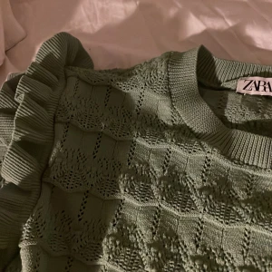 Grön stickad tröja med volang från Zara - Säljer en ljusgrön stickad tröja från Zara med volangdetaljer på axlarna. Tröjan har ett diskret rutmönster och långa ärmar. Perfekt för dig som vill ha något unikt och snyggt i garderoben!